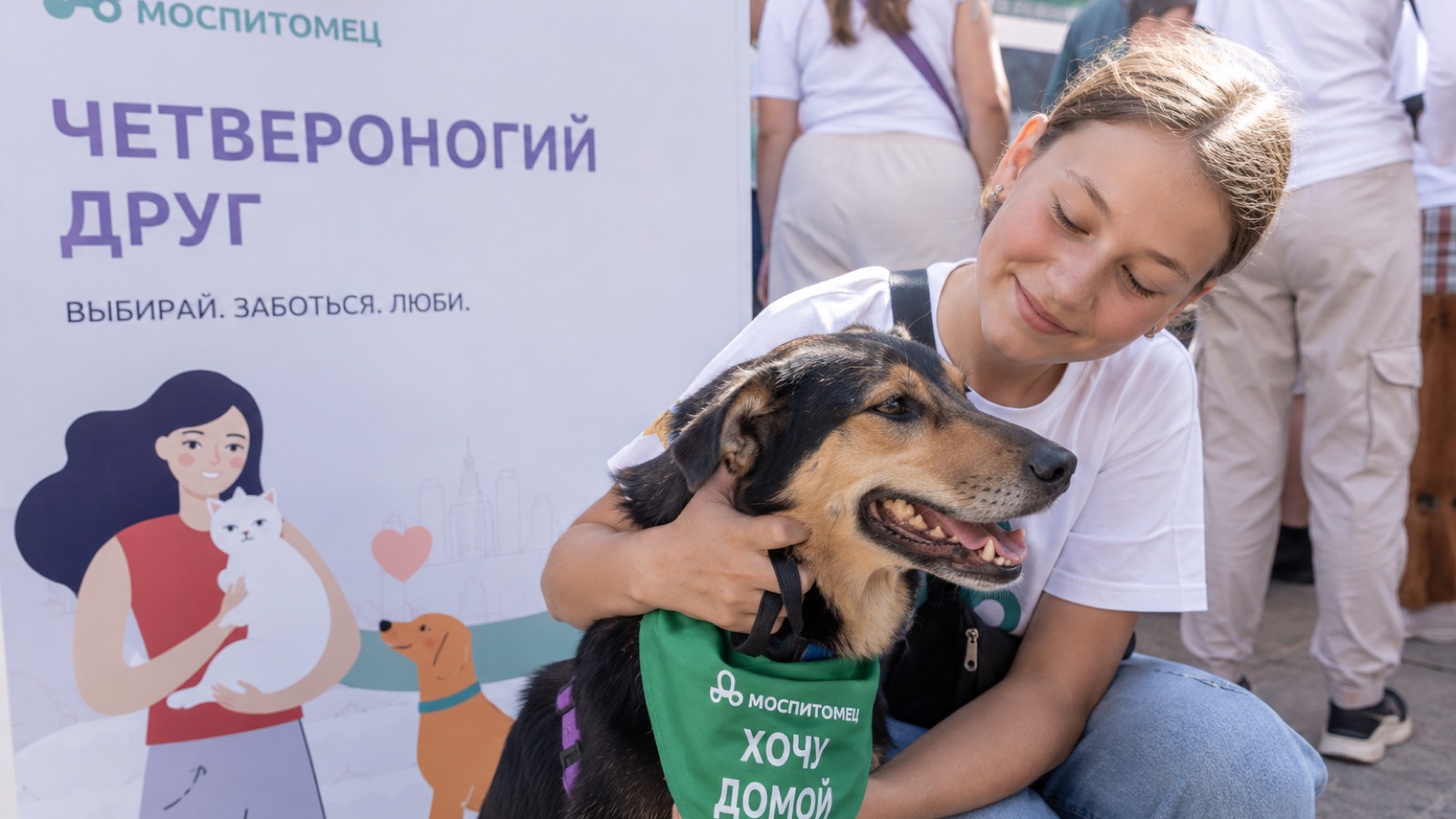 Девушка обнимает собаку из приюта в бандане «Хочу домой» на фестивале «Моспитомец»